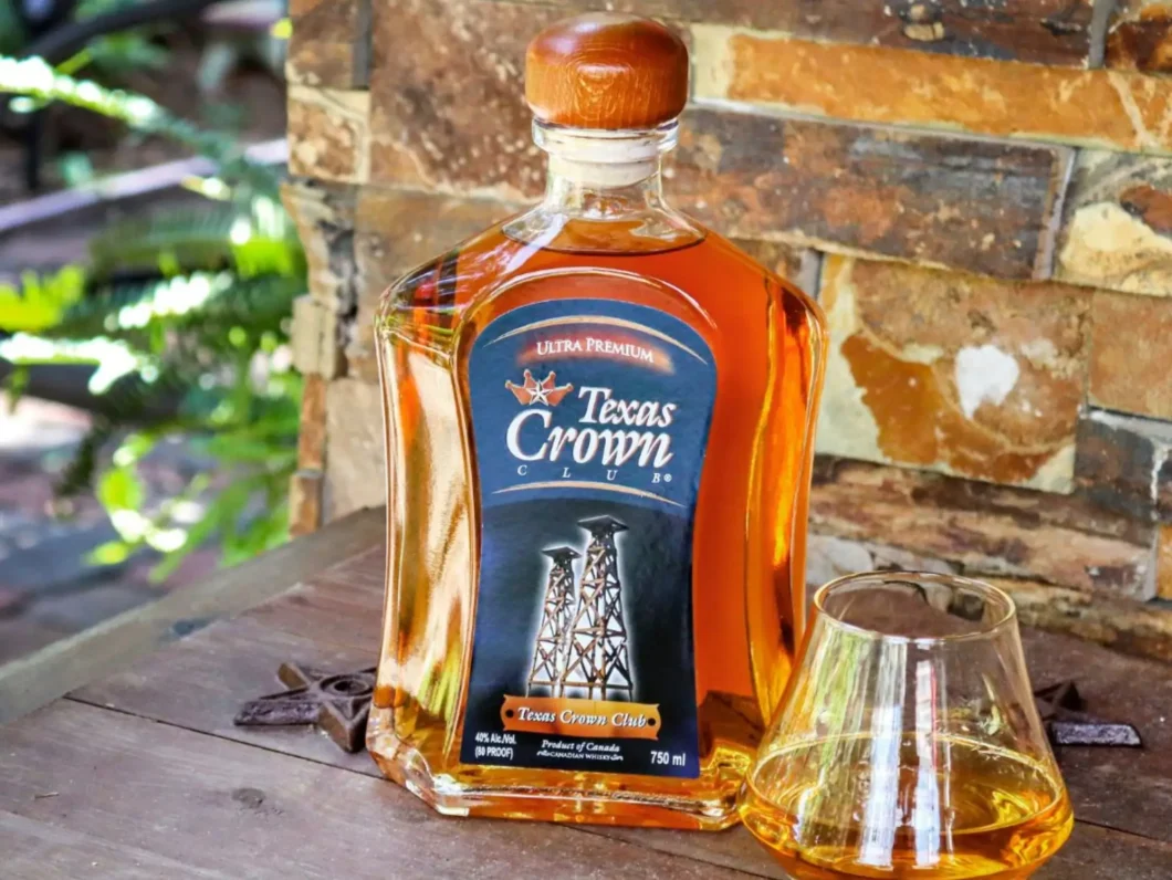 A bottle of Texas Crown Club Whisky on a wooden table outside during a bright sunny day.