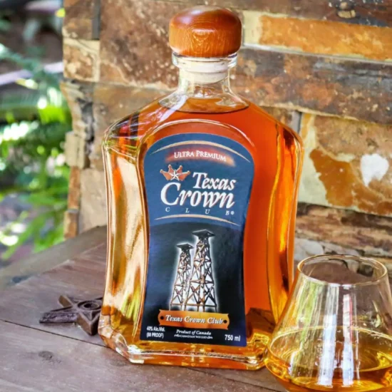 A bottle of Texas Crown Club Whisky on a wooden table outside during a bright sunny day.